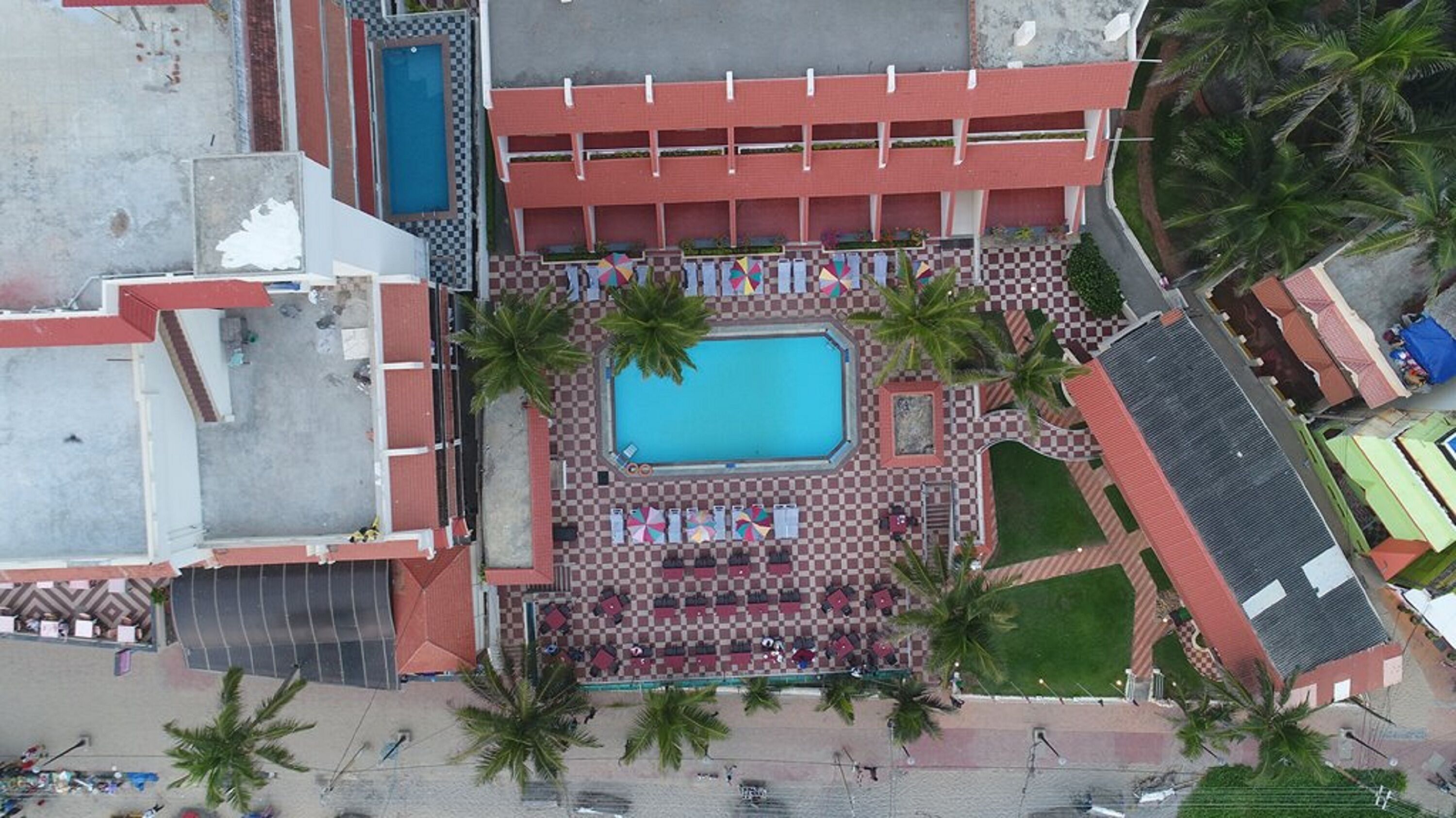Vue aérienne d’un hôtel doté d’une piscine centrale, de plusieurs étages et d’un motif à carreaux autour de la piscine.
