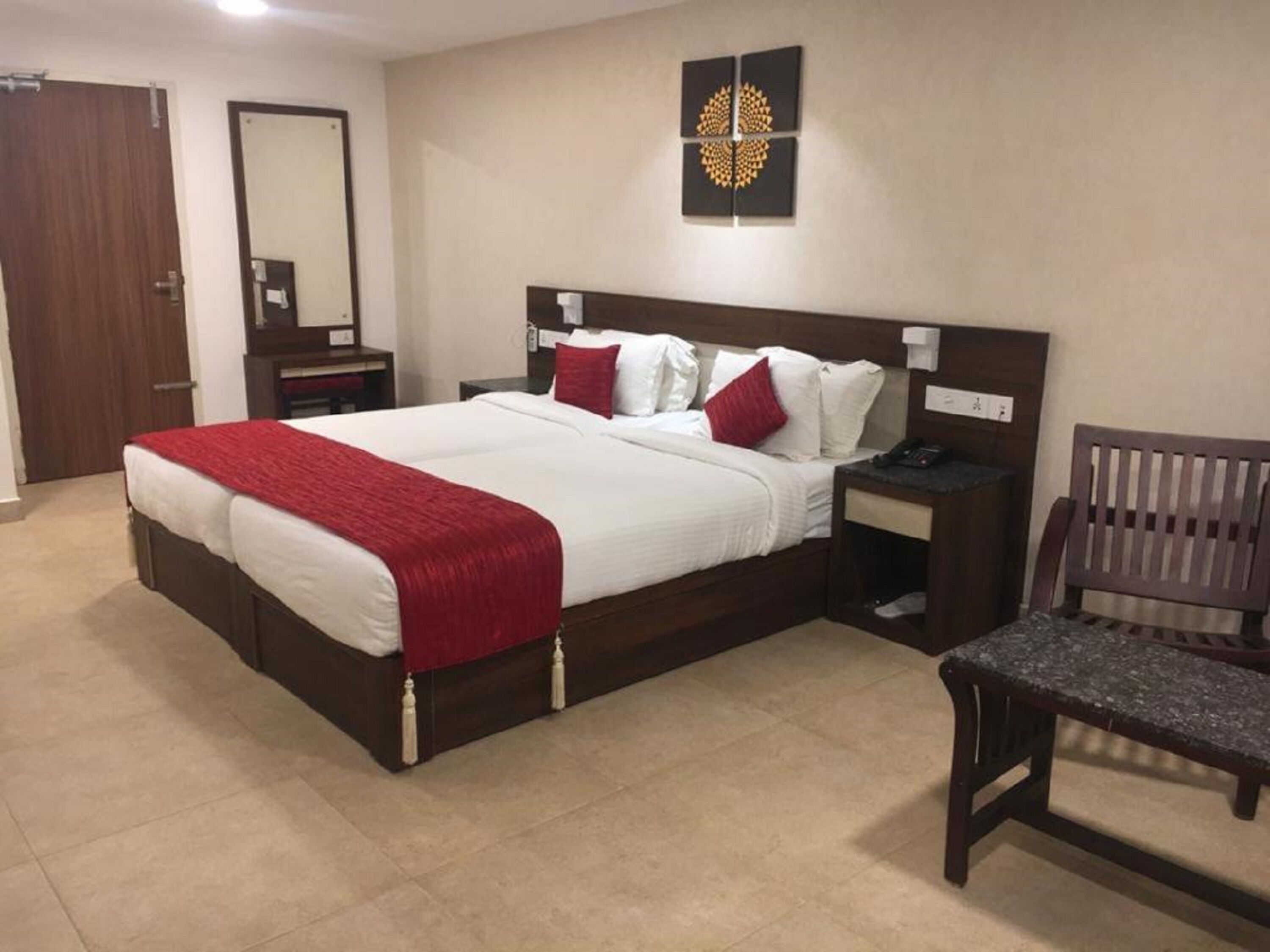A double bed with a red throw blanket, a wooden nightstand with a phone, a chair, and a wall-mounted artwork.
