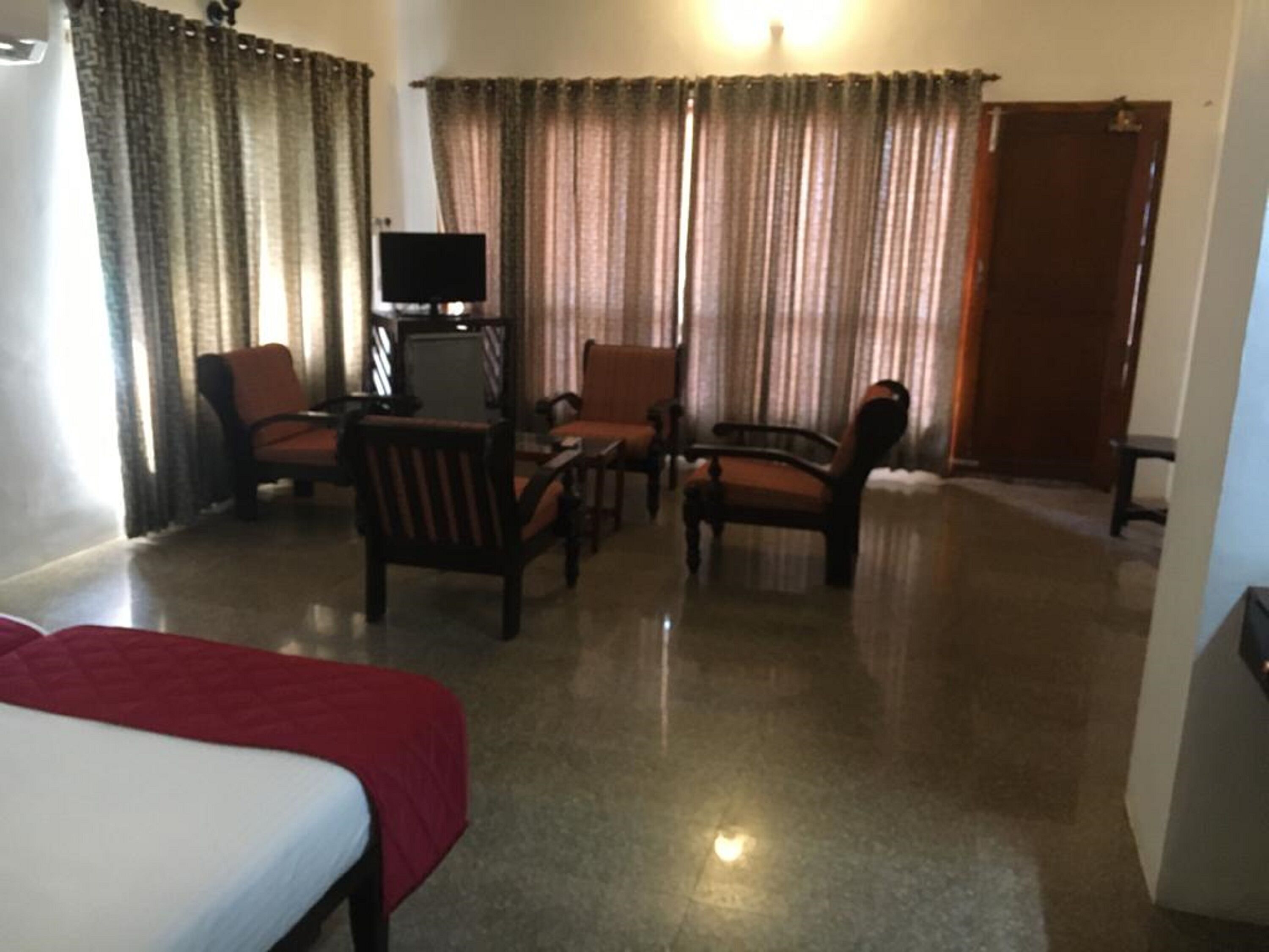 A hotel room with a bed, a desk, two chairs, a television, and curtains.