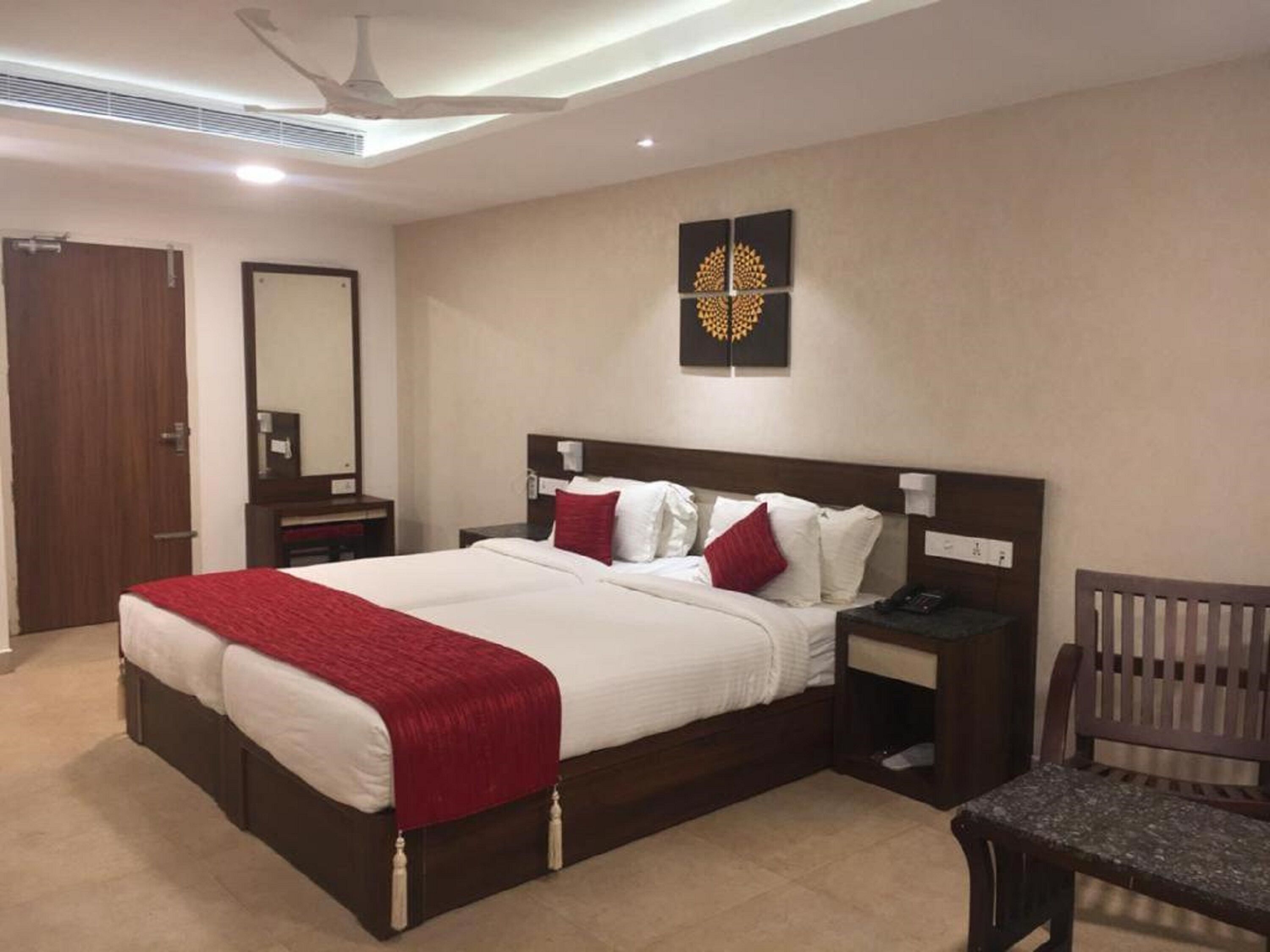 Een hotelkamer met een groot bed, een houten hoofdeinde, een nachtkastje, een stoel en een plafondventilator.