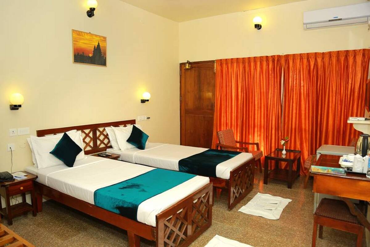 A hotel room with two beds, a desk, a chair, and a large window with orange curtains.