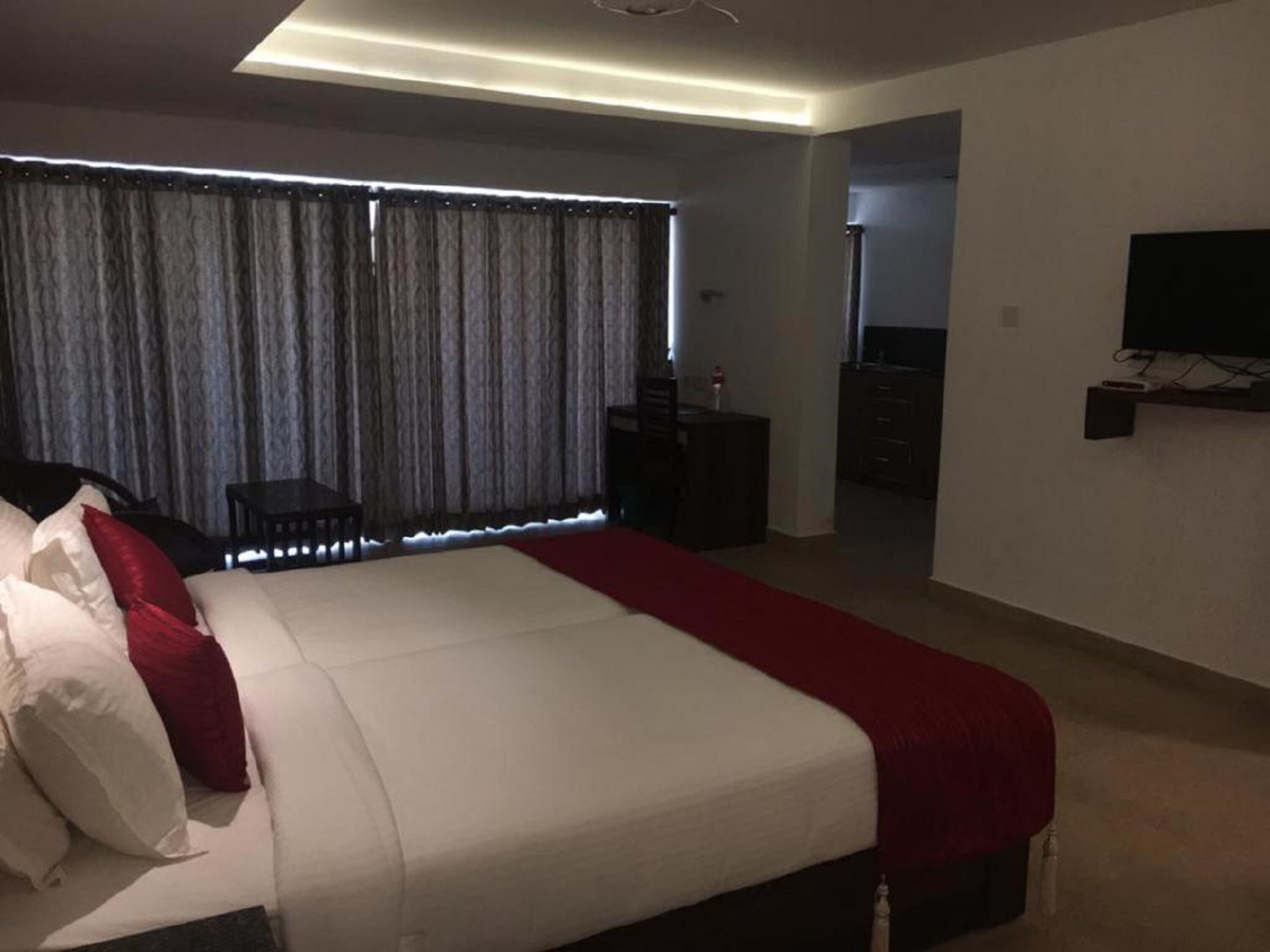 A bedroom with a large bed, a TV mounted on the wall, and a desk with a chair.
