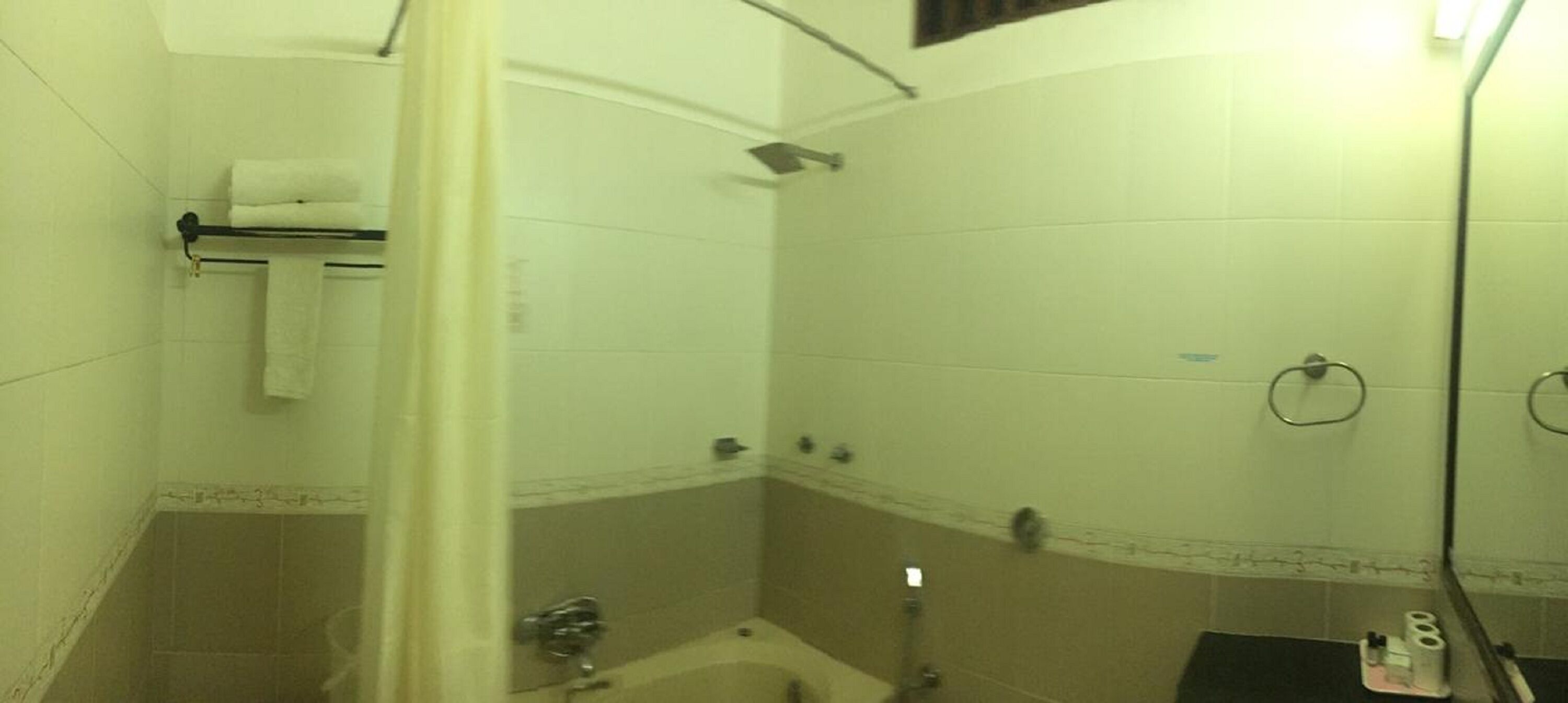Une petite salle de bain carrelée, équipée d’une douche, d’un lavabo et de toilettes.
