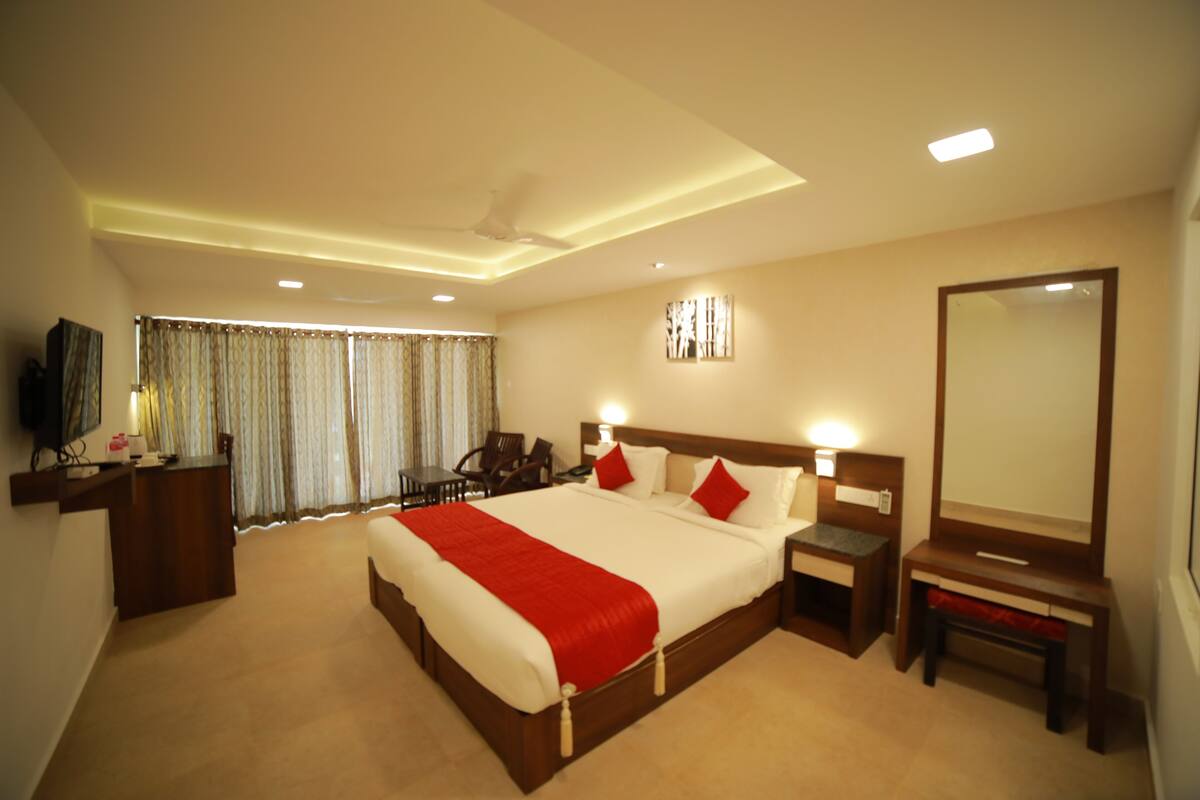 A hotel room with a large bed, bedside tables, a desk, a chair, a TV, and curtains.