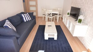 A living room with a dark blue sofa, a white coffee table, and a TV on a white stand. - Victus Apartamenty - Marina (Sopot)