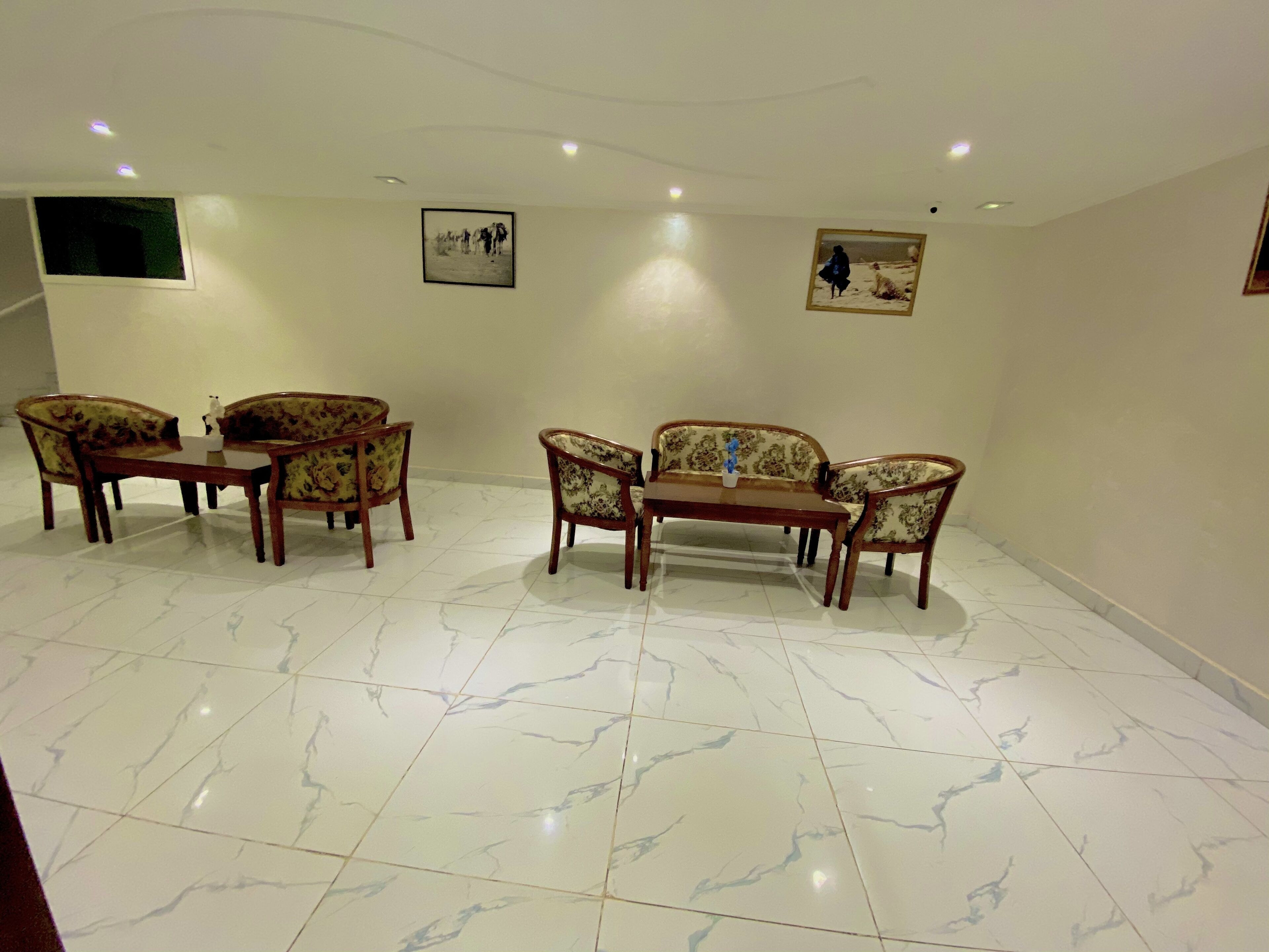 Una habitación con piso de mármol, dos mesas de comedor con sillas y dos sofás.