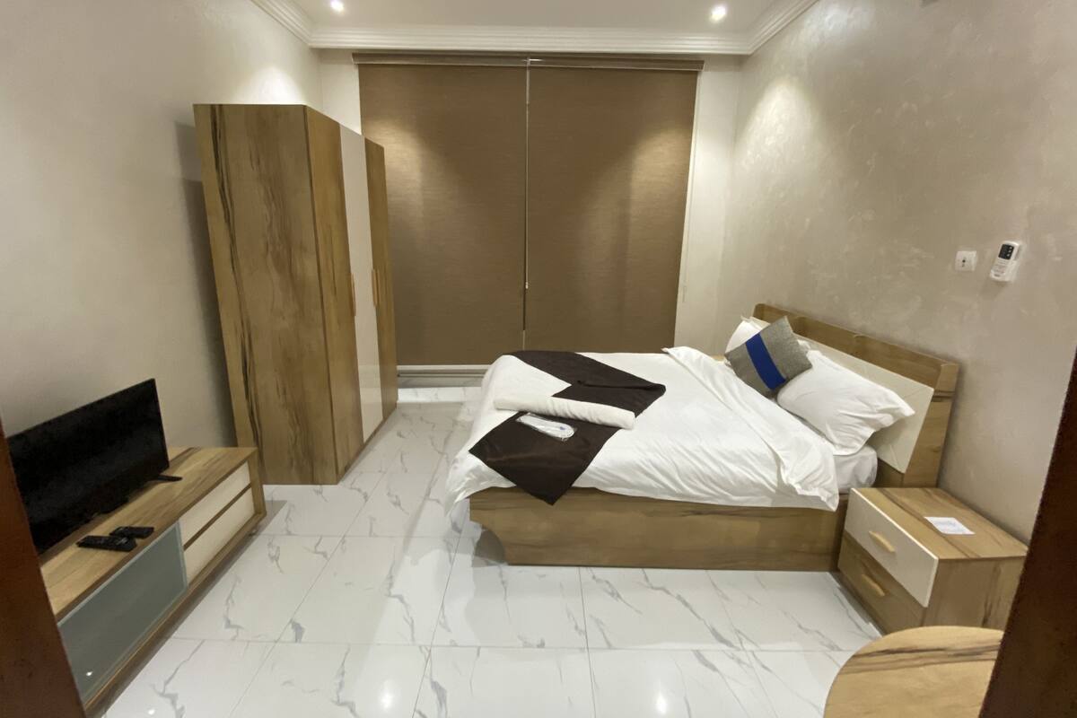 A modern hotel room with a bed, wooden wardrobe, a TV, and a marble floor.