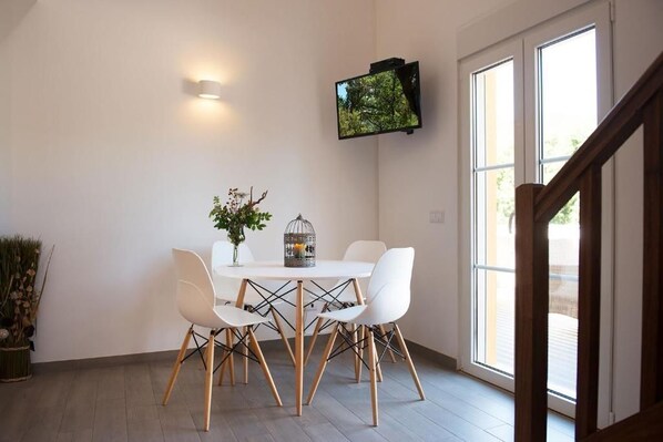 A dining area with a white table and chairs, a decorative plant, and a television mounted on the wall.