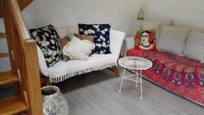 Una sala de estar acogedora con un sofá blanco, cojines estampados, una mesita blanca y una alfombra colorida.