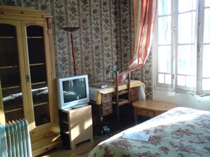 A bedroom with a wooden wardrobe, a desk with a chair, a bed with a floral bedspread, and a window with curtains. - Domaine des Plantes (Rennes)