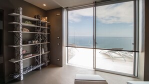 A modern room with a large sliding glass door to a balcony overlooking the sea, a white bookshelf, and a simple seating area. - Capo Torre Resort (Albisola Superiore)