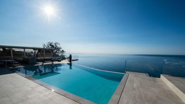 A clear blue pool with a view of the sea, a covered seating area, and a tiled deck. - Capo Torre Resort (Albisola Superiore)