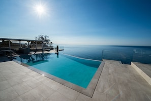 A clear blue pool with a view of the sea, a covered seating area, and a tiled deck. - Capo Torre Resort (Albisola Superiore)