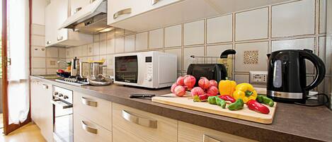 A modern kitchen with a microwave, coffee maker, and a cutting board with vegetables.