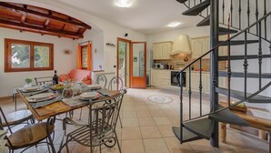 A dining area with a wooden table and chairs, a kitchen with white cabinets, and a black spiral staircase. - Villa Monte Enrico - With Pool (Camporosso)