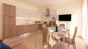 A modern kitchen with built-in appliances, a dining area with a table and chairs, and a flat-screen TV mounted on the wall. - Serena 2 (Alassio)