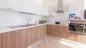A modern kitchen with white cabinets, stainless steel appliances, and a microwave. - Serena 2 (Alassio)