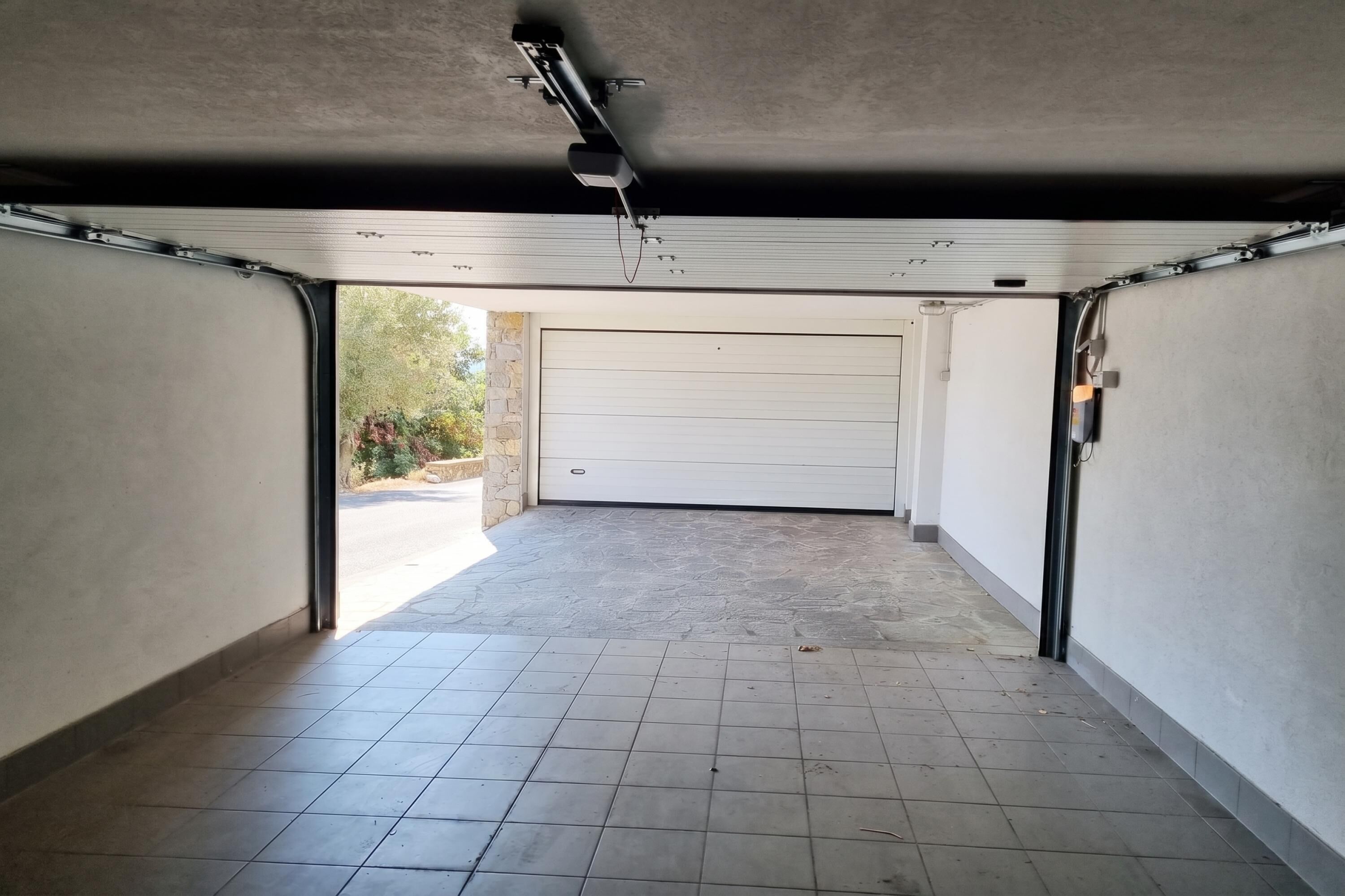 A garage with a white door, a tiled floor, and a ceiling light fixture.