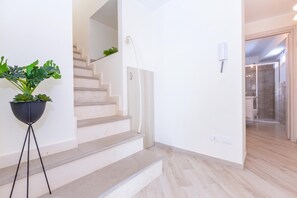 A staircase leading to a second floor, a potted plant, and a bathroom with a shower and toilet.