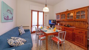 A dining area with a table set for four, a blue sofa with patterned cushions, a wooden cabinet with glass doors, and a television on a stand.