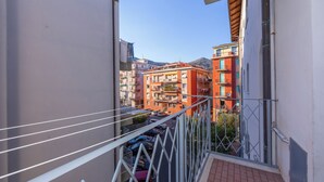 A balcony with a metal railing overlooking a street with parked cars and buildings in the background.