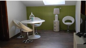 A small, modern room with a round table, two chairs, a birdcage, a lamp, and a toilet.