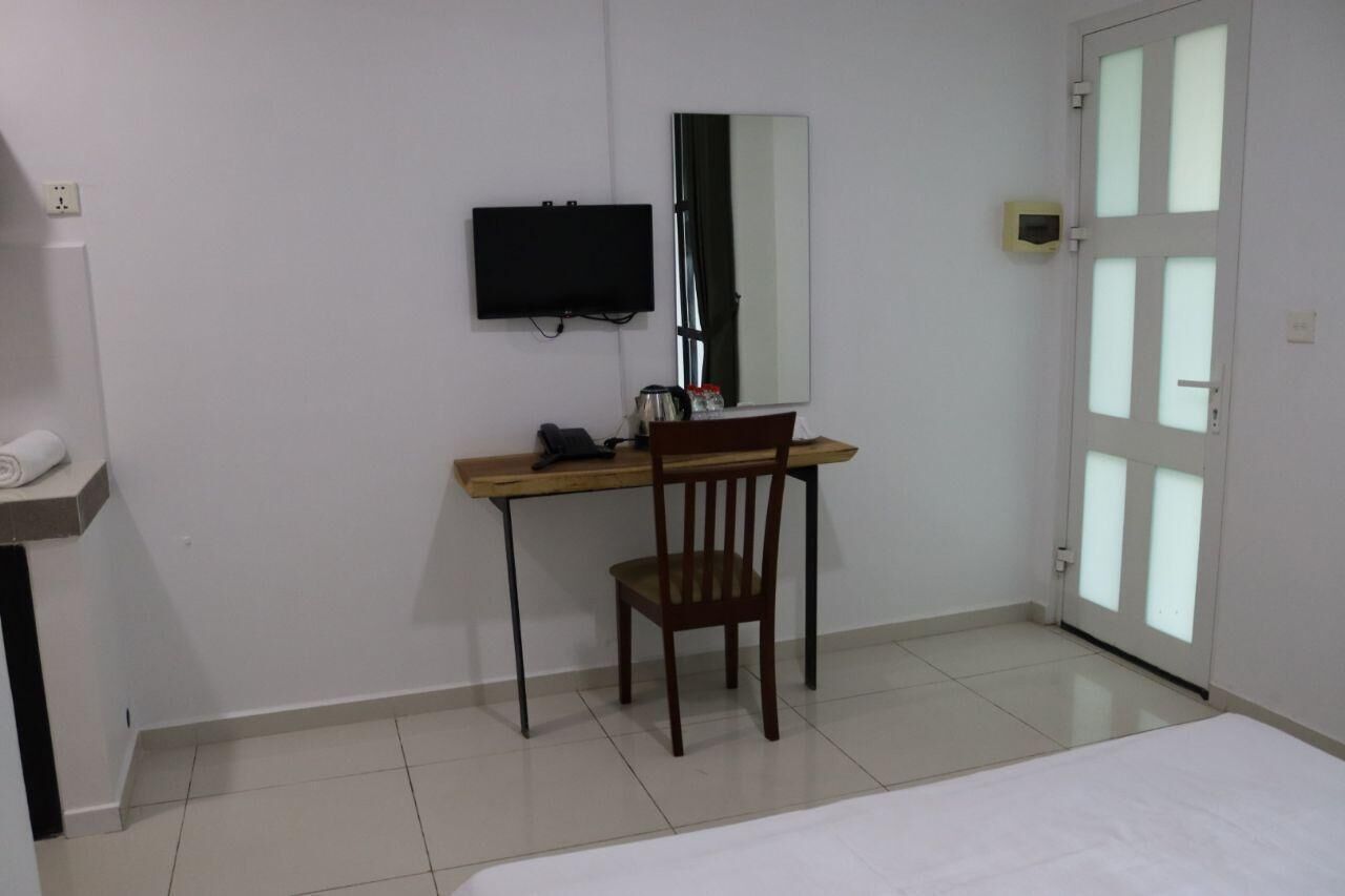 A hotel room with a bed, a desk with a chair, a flat-screen TV, a mirror, and a door with frosted glass panels.