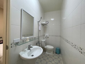 A small, clean bathroom with a white sink, a toilet, and a glass shelf above the sink.
