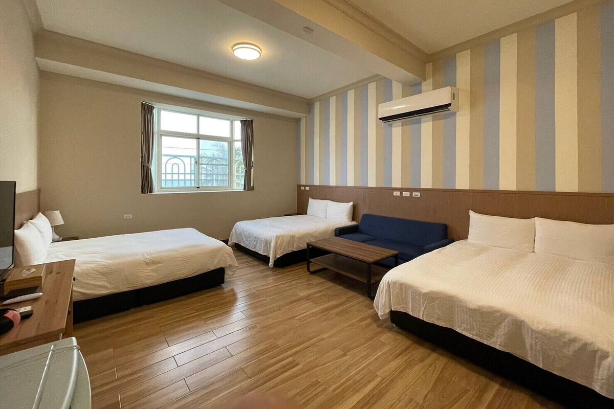 A hotel room with two single beds, a sofa, a desk, and a window with curtains.