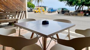 An outdoor seating area with a table and chairs, a wooden wall, and a view of the street with parked cars and palm trees. - Small Ryukyu Loju sunrise Inn (Liuqiu)