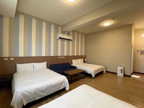 A hotel room with two single beds, a wooden headboard, a small table, a bedside lamp, and a wall-mounted air conditioner.