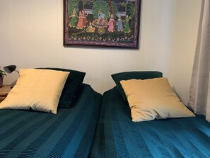 A room with two beds, each with a green bedspread and a yellow pillow. A framed artwork depicting a traditional scene hangs on the wall above the beds. - Reykjavik Guesthouse (Reykjavik)