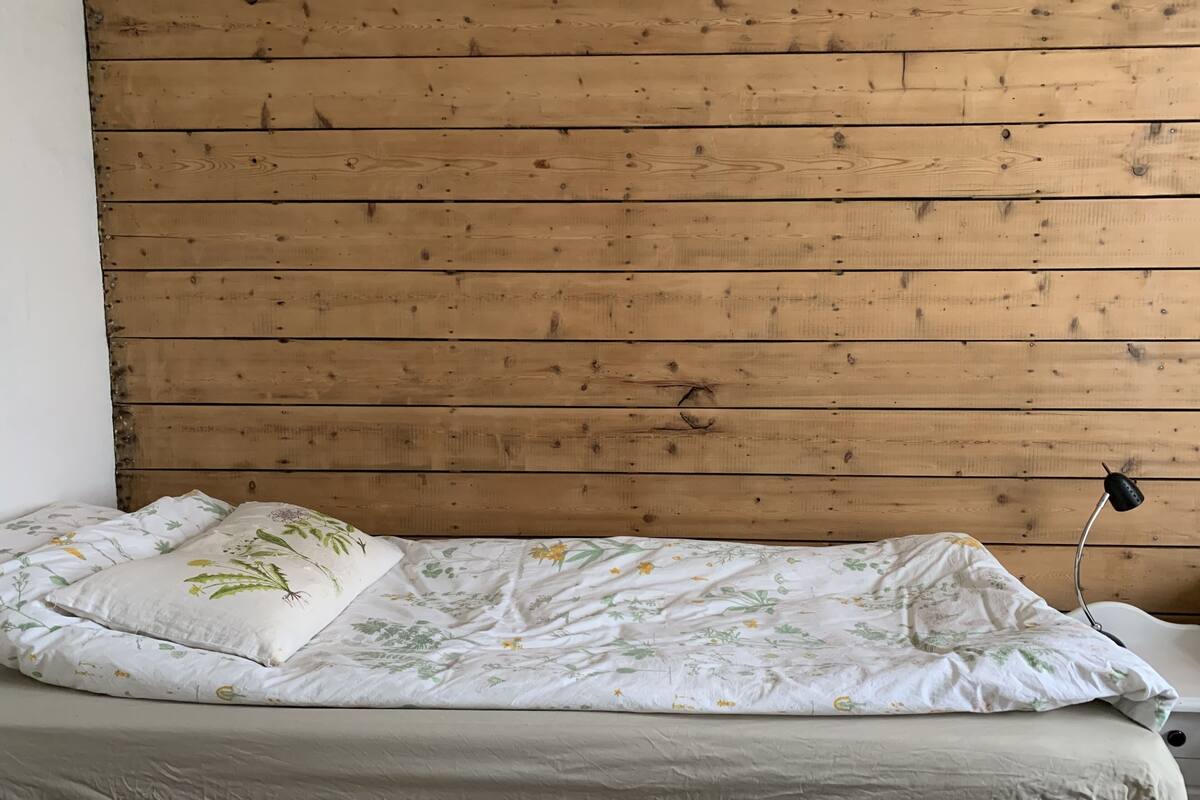 A single bed with floral bedding against a wooden headboard.