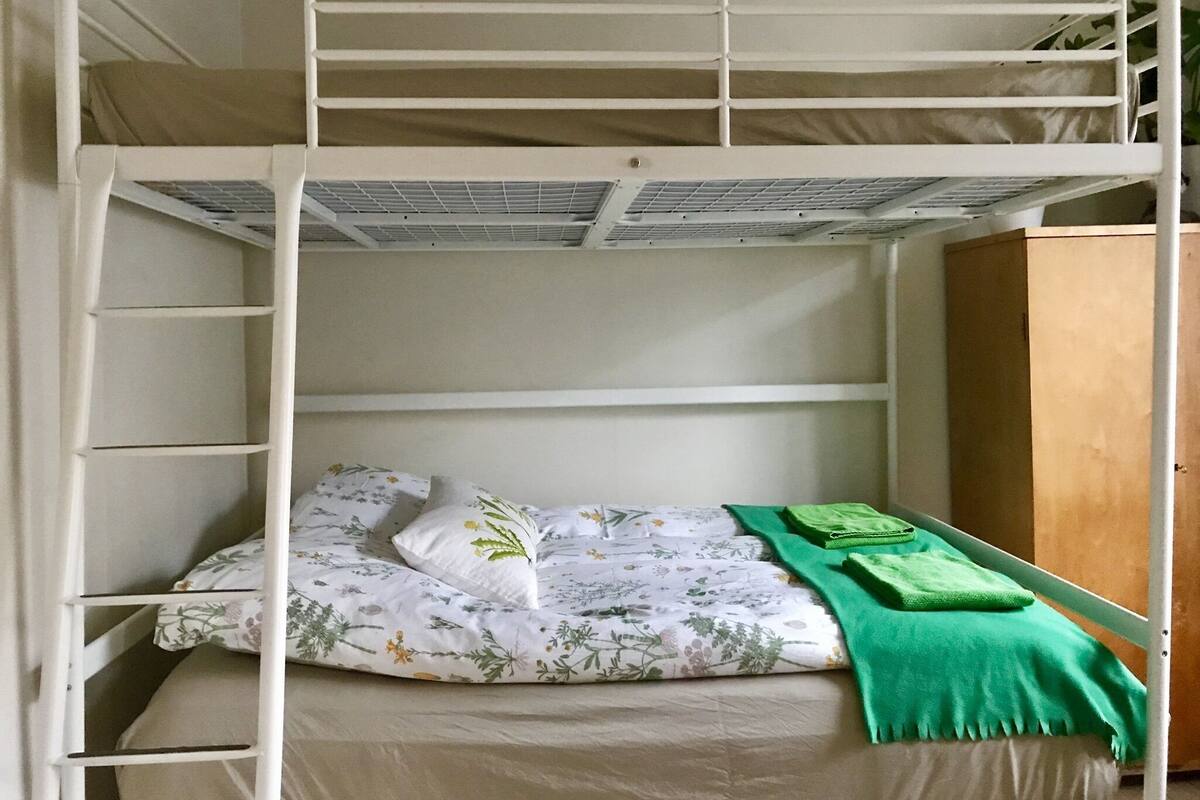 A bunk bed with a lower bunk, a wooden wardrobe, and a green blanket on the top bunk.