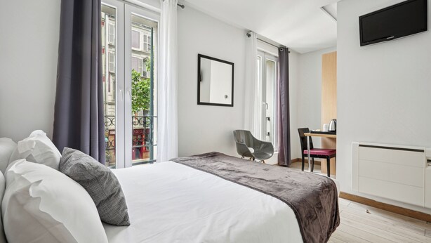 A modern hotel room with a large bed, a desk, a chair, and a TV. - Hotel Le National Clichy Paris (Clichy)