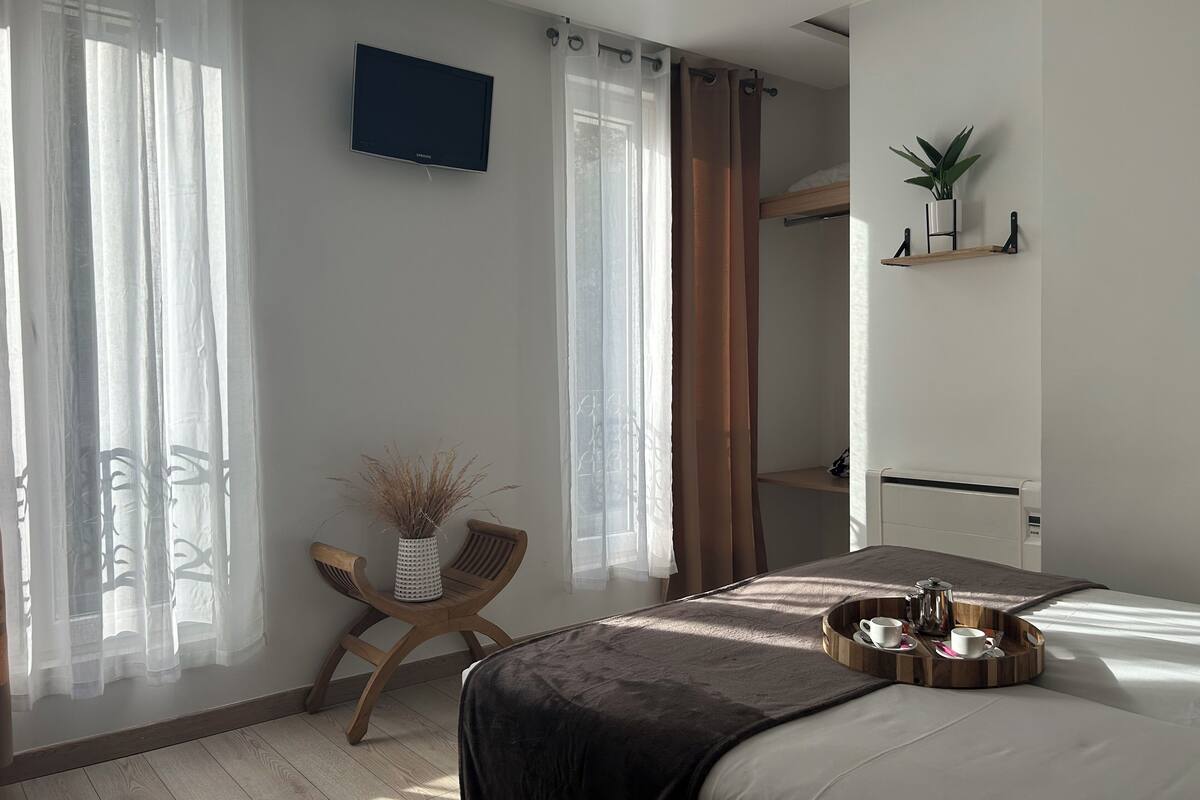 A modern bedroom with a bed, a TV mounted on the wall, a small table with a tray of items, and a chair.