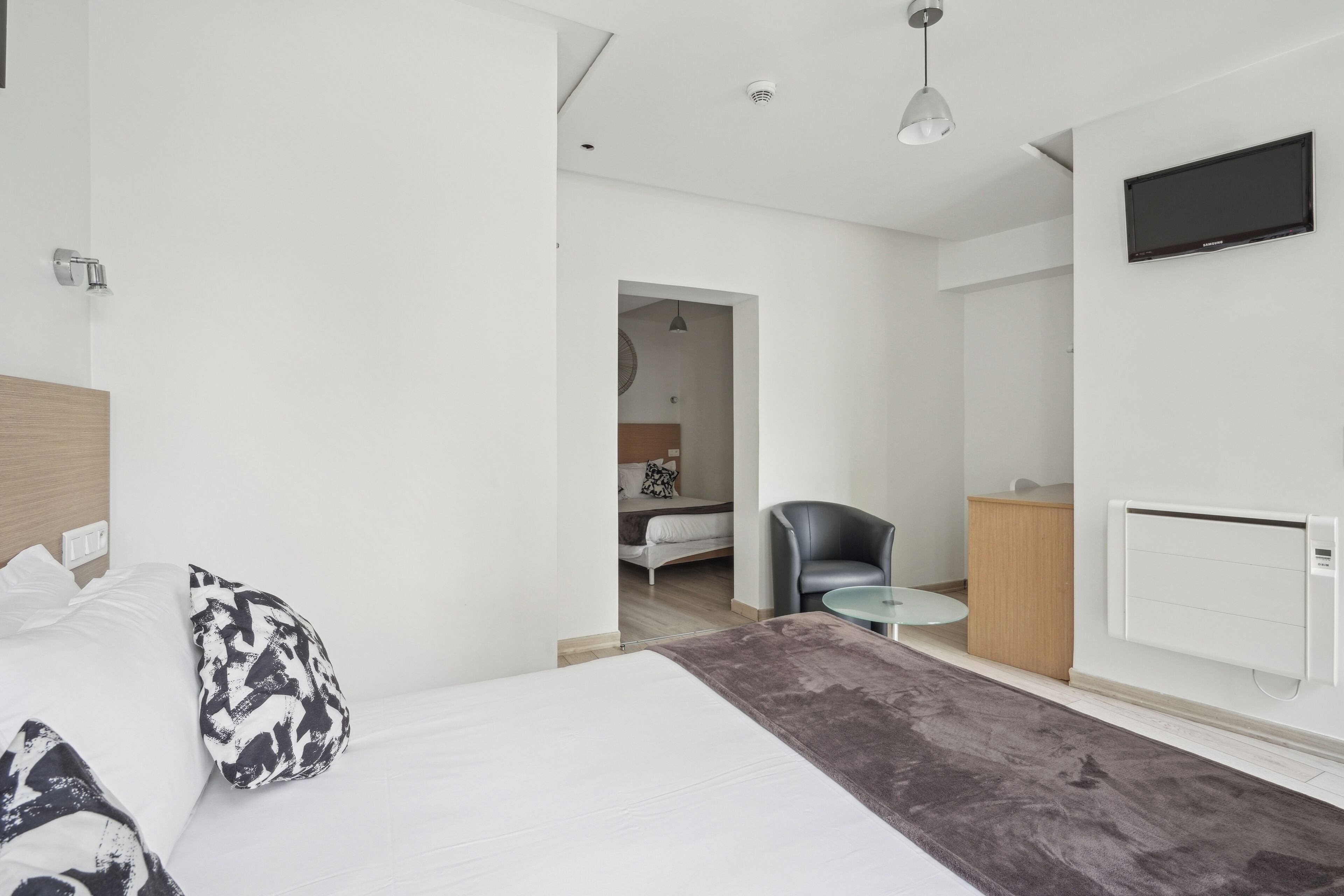 A modern hotel room with a large bed, a desk, a chair, and a TV.