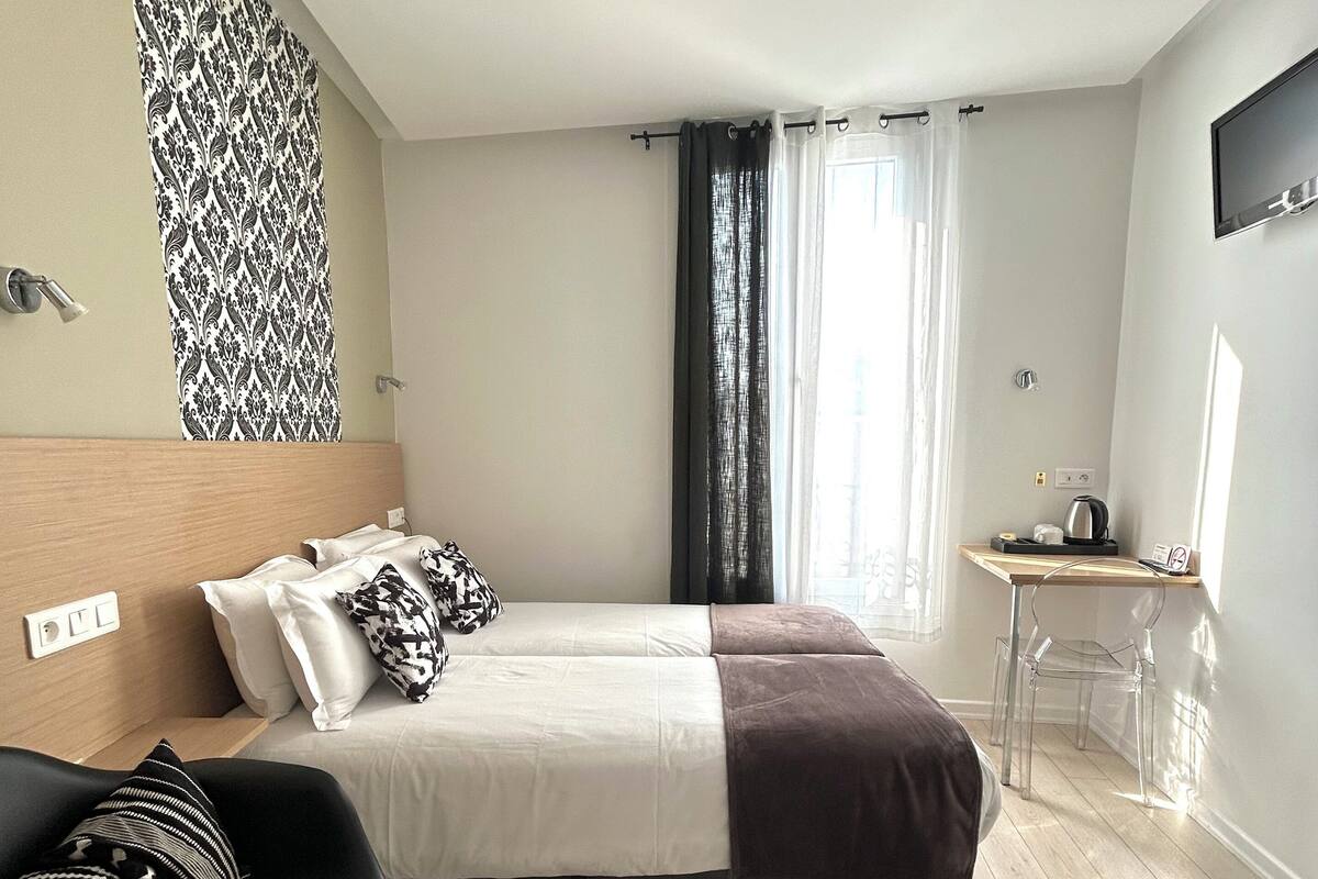 A modern bedroom with a bed, a desk, a chair, and a TV.