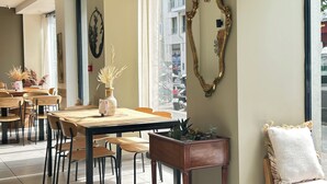 A modern interior with a long table and chairs, a decorative mirror, and a window with a view of the street. - Hotel Le National Clichy Paris (Clichy)