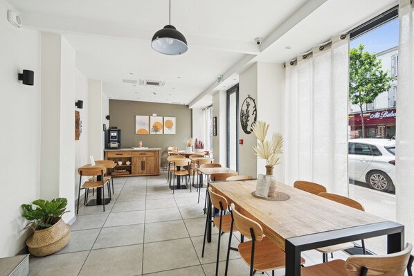 A modern cafe with wooden tables and chairs, a central counter, and artwork on the walls.