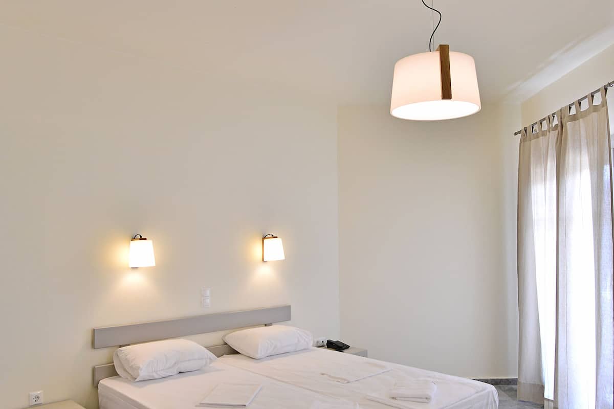 Une chambre d’hôtel moderne avec un grand lit, deux tables de chevet et un luminaire suspendu.