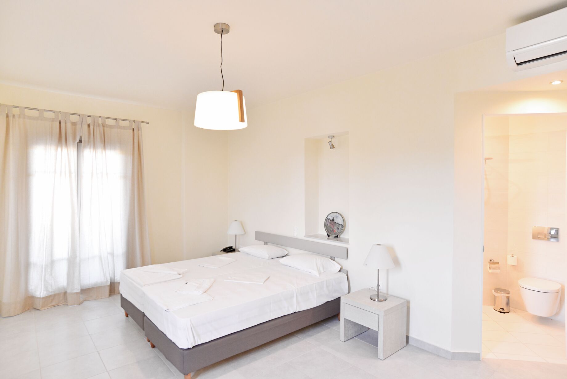 Una habitación de hotel moderna con cama, mesita de noche y baño visible a través de una puerta abierta.