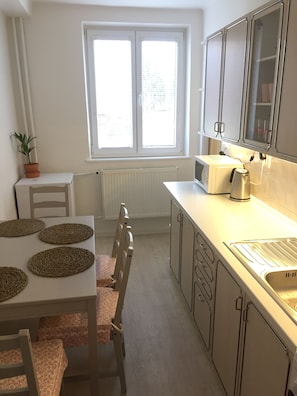 A compact kitchen with a window, white cabinets, a microwave, and a kettle.