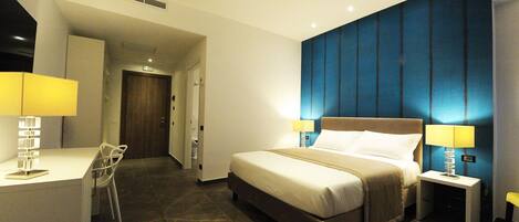 Habitación de hotel con cama, lámparas de noche, escritorio con silla y baño visible a través de una puerta abierta.
