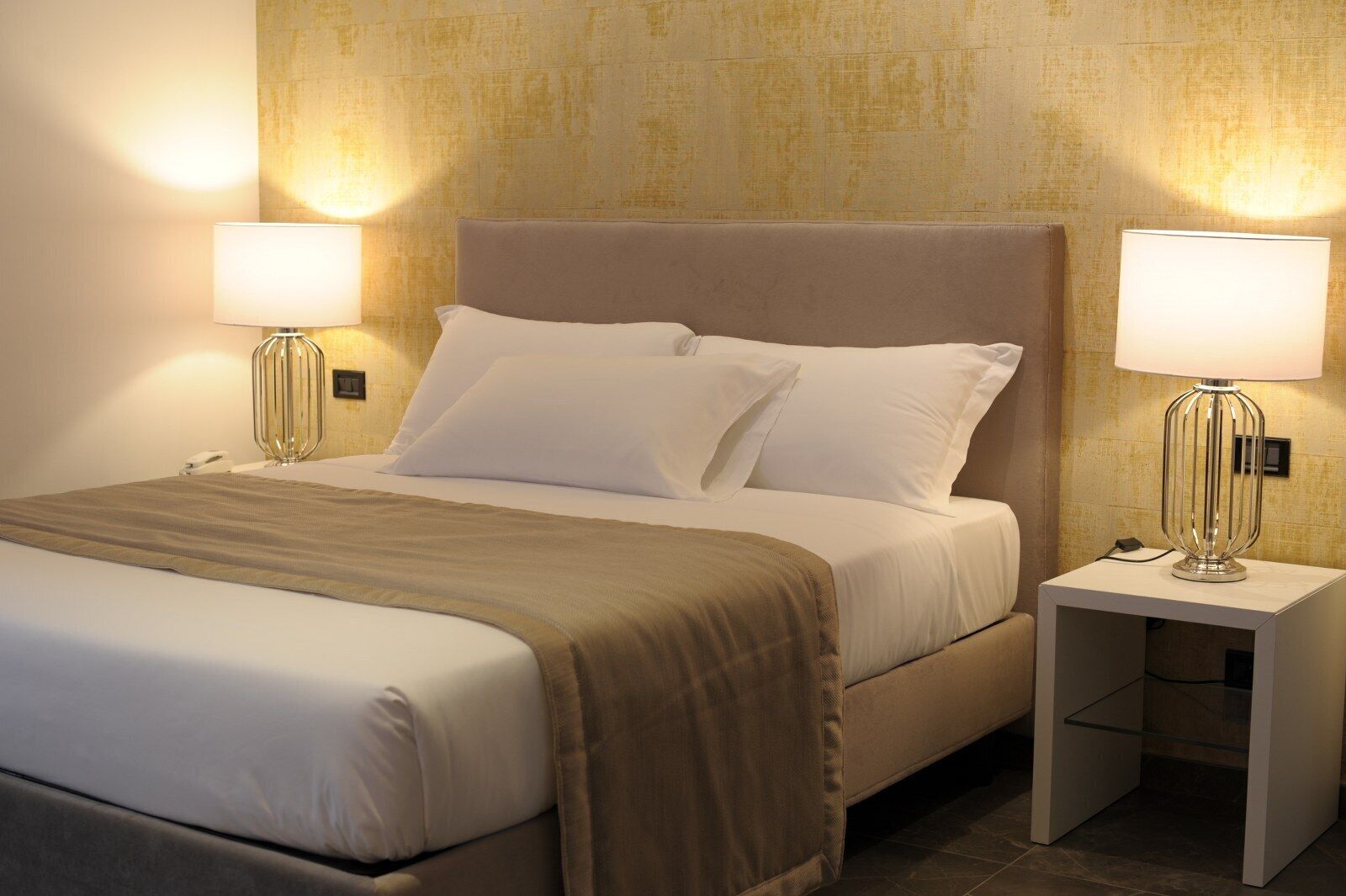 A hotel room with a bed, two bedside tables with lamps, and a textured wall.