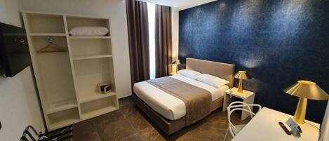 A modern hotel room with a large bed, a desk with a lamp, a wardrobe, and a TV.