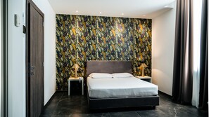 A modern bedroom with a large bed, two bedside tables with lamps, a patterned wallpaper, and a dark floor. - Hotel Up Museum - Wellness & Spa (Foggia)