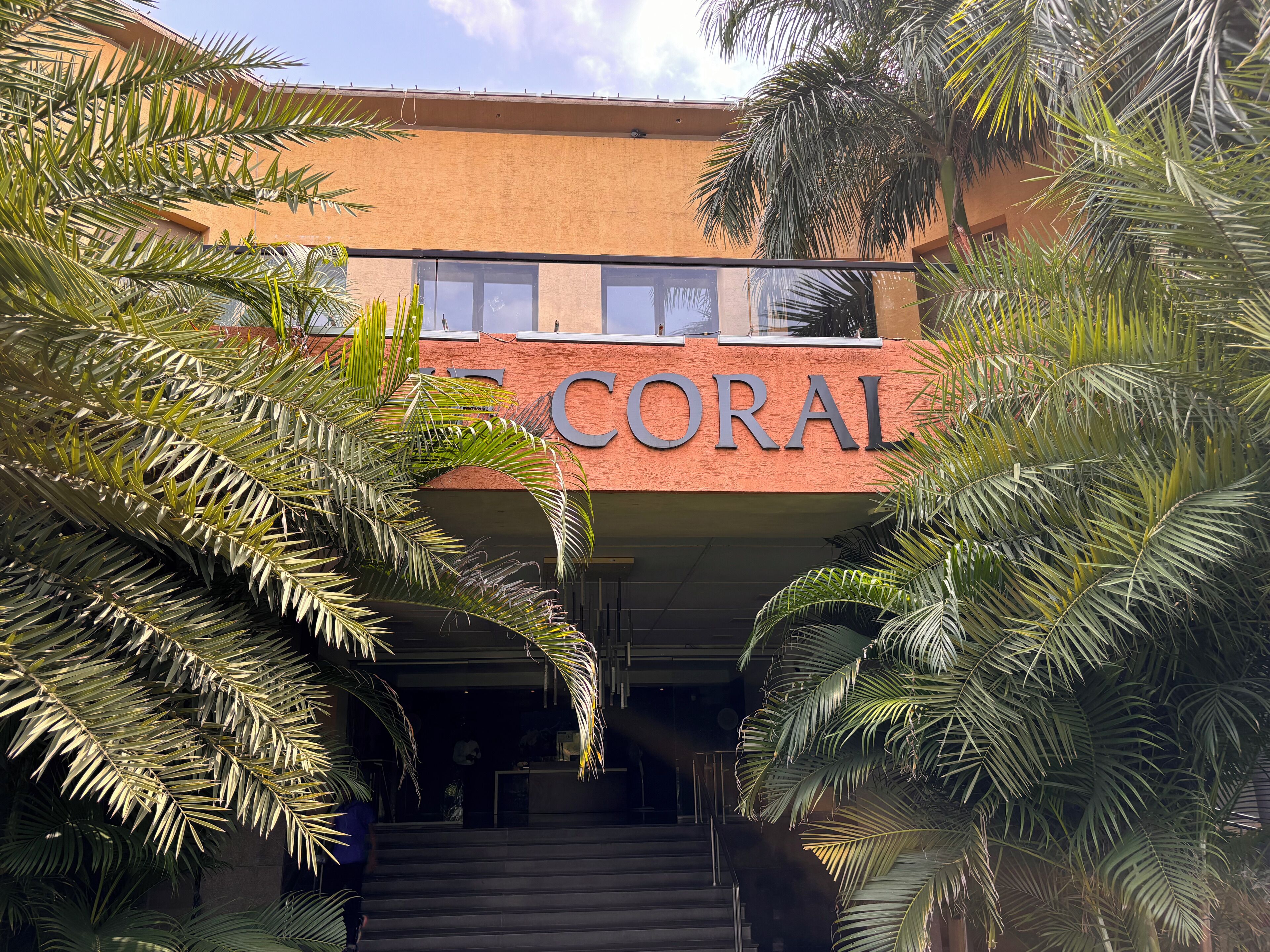 A building with the sign "CORAL" above the entrance, surrounded by palm trees.