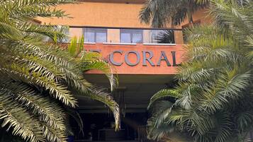 A building with the sign "CORAL" above the entrance, surrounded by palm trees.
