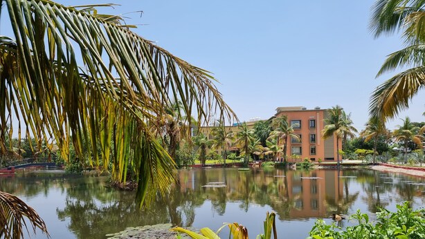 A serene hotel pool with palm trees and a building in the background. - Palm Green Club & Resort by The Sky Imperial (Kheda)